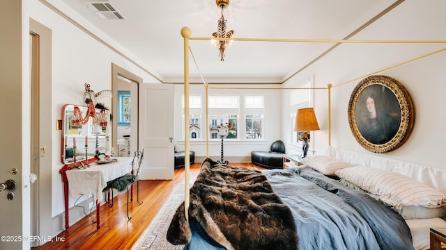 bedroom featuring visible vents, ornamental molding, light wood-style flooring, and an inviting chandelier