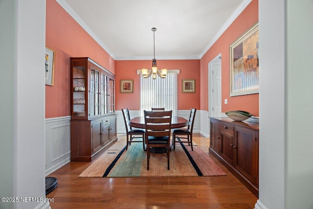 dining area featuring a wainscoted wall, crown molding, wood finished floors, and a notable chandelier