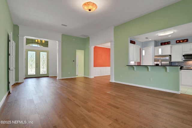 unfurnished living room featuring visible vents, light wood-type flooring, decorative columns, a chandelier, and french doors
