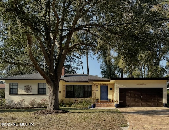 ranch-style house with a garage, decorative driveway, brick siding, and a chimney