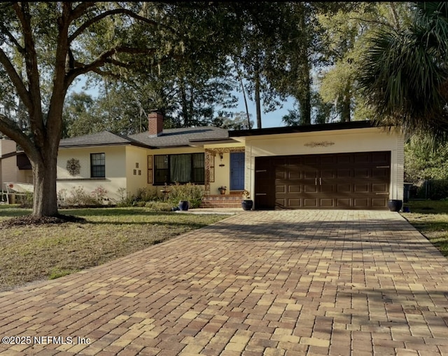 ranch-style house featuring a garage, a chimney, decorative driveway, and stucco siding