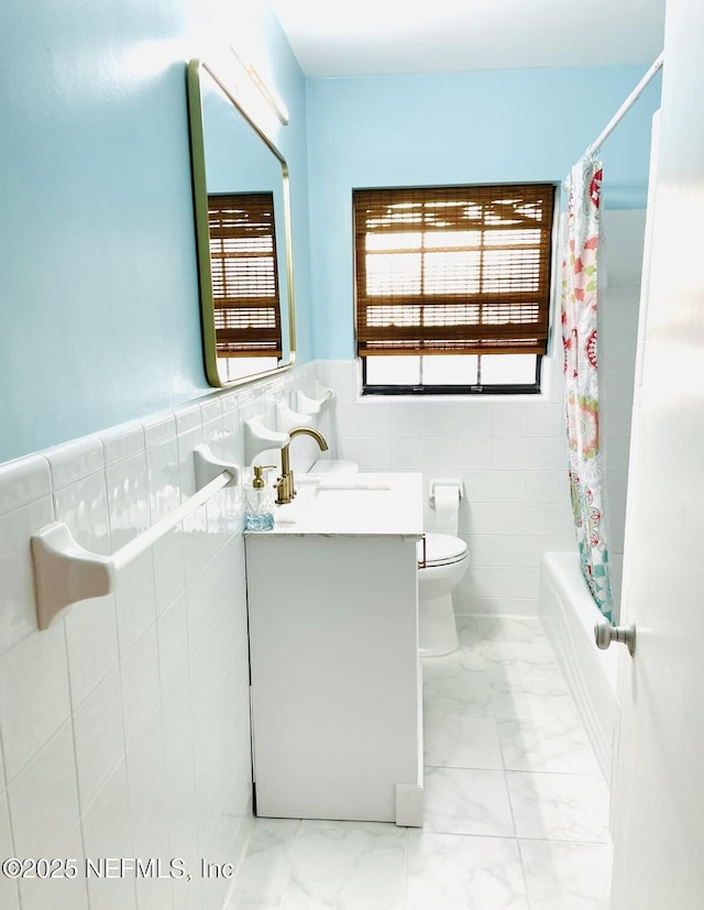 full bath with toilet, vanity, tile walls, marble finish floor, and wainscoting