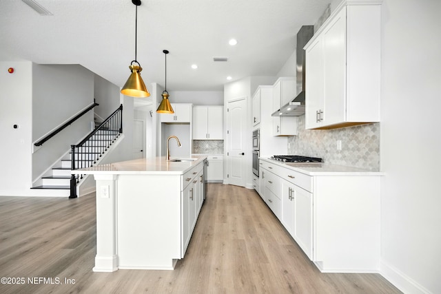 41 Iris Creek Dr, Saint Augustine, FL 32092 - kitchen with appliances with stainless steel finishes, wall chimney exhaust hood, light wood-style floors, white cabinetry, and backsplash