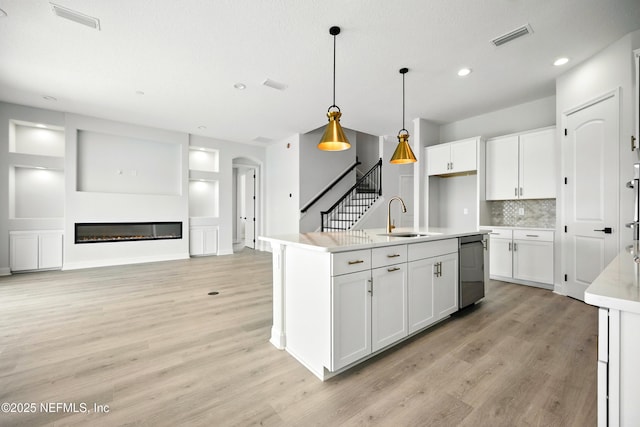41 Iris Creek Dr, Saint Augustine, FL 32092 - kitchen with light wood-style flooring, tasteful backsplash, white cabinetry, hanging light fixtures, and a glass covered fireplace