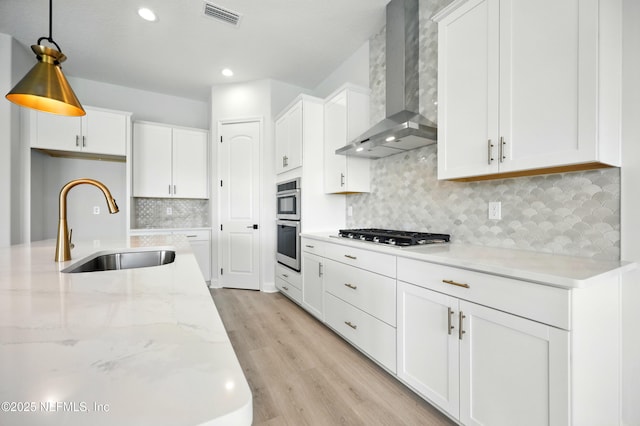 41 Iris Creek Dr, Saint Augustine, FL 32092 - kitchen with wall chimney exhaust hood, stainless steel appliances, white cabinetry, light wood finished floors, and decorative light fixtures