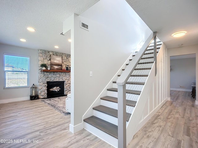 stairs featuring a fireplace, visible vents, a textured ceiling, wood finished floors, and baseboards