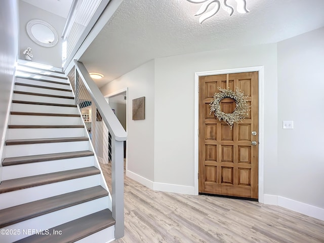 foyer featuring stairs, a textured ceiling, light wood-style flooring, and baseboards