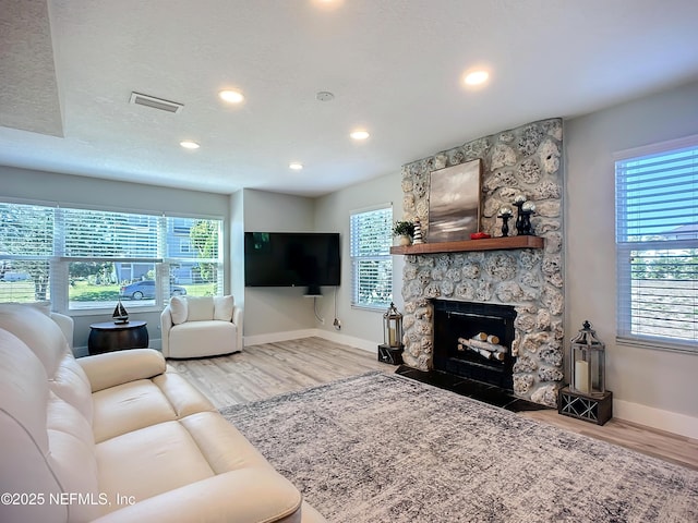 living area with a fireplace, visible vents, a textured ceiling, wood finished floors, and baseboards