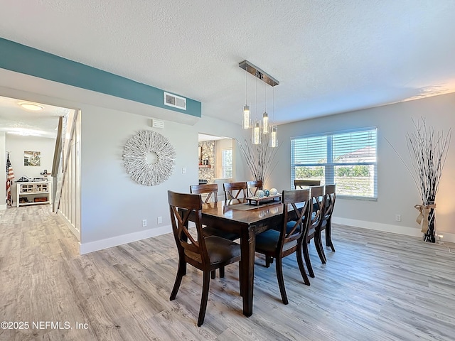 dining area with light wood-type flooring, baseboards, visible vents, and a textured ceiling