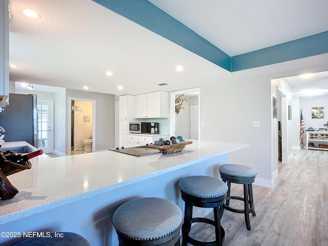 kitchen featuring white cabinetry, a kitchen breakfast bar, appliances with stainless steel finishes, light stone countertops, and light wood finished floors