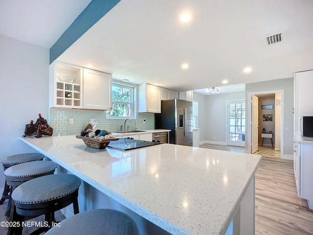 kitchen with stainless steel appliances, visible vents, backsplash, a peninsula, and a kitchen bar