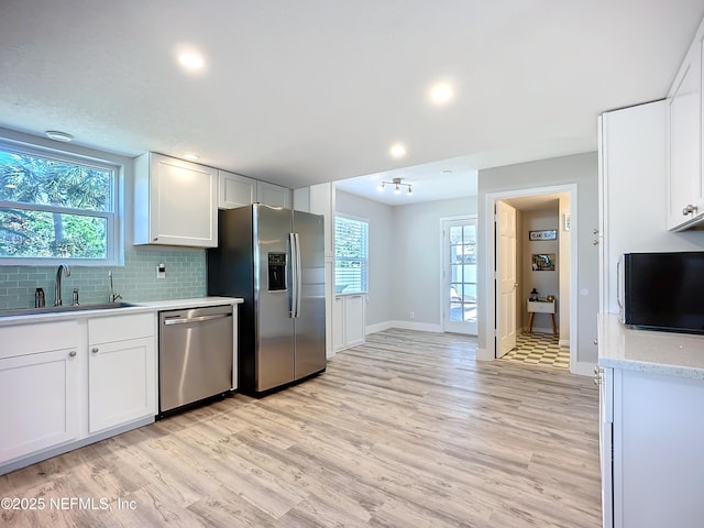 kitchen with decorative backsplash, appliances with stainless steel finishes, light wood-style floors, white cabinetry, and a sink