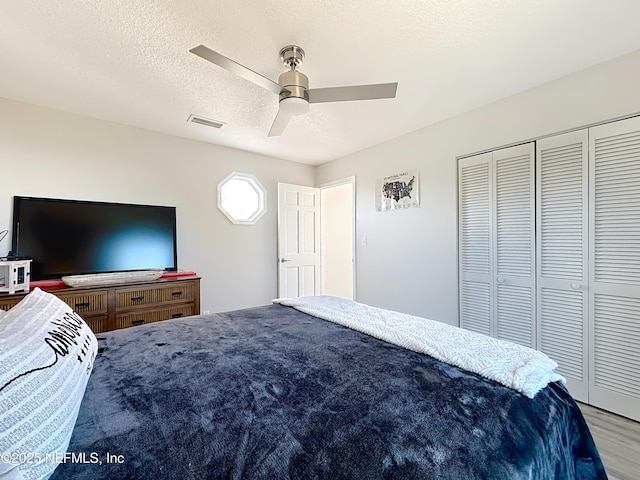 bedroom featuring a textured ceiling, wood finished floors, visible vents, a ceiling fan, and a closet