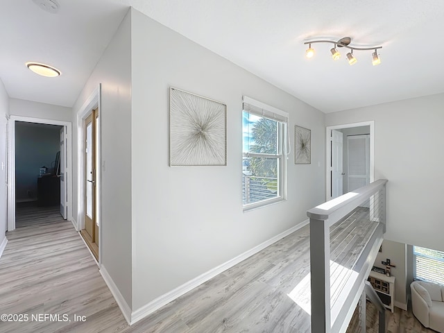 corridor featuring light wood-style floors, a wealth of natural light, and baseboards