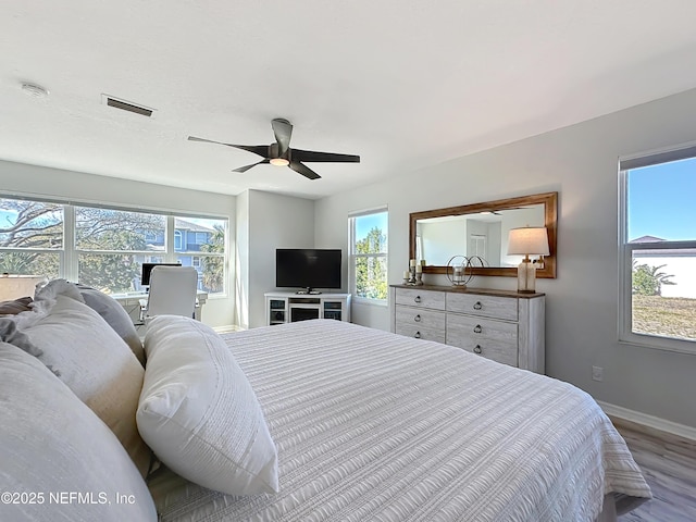 bedroom with multiple windows, wood finished floors, visible vents, and baseboards