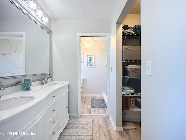 full bathroom featuring double vanity, a textured ceiling, a sink, and wood finished floors