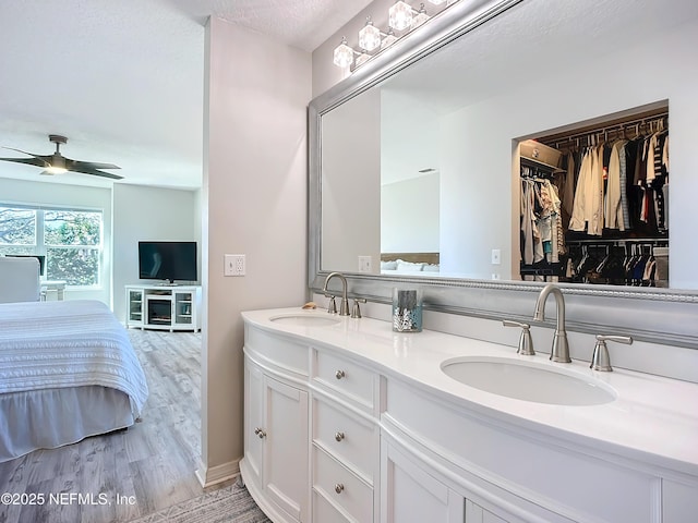 bathroom with ceiling fan, connected bathroom, a sink, and wood finished floors