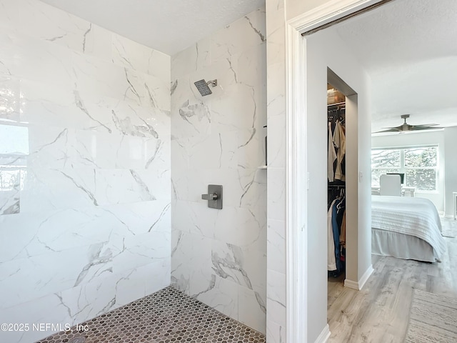 bathroom featuring ceiling fan, tiled shower, wood finished floors, and a walk in closet