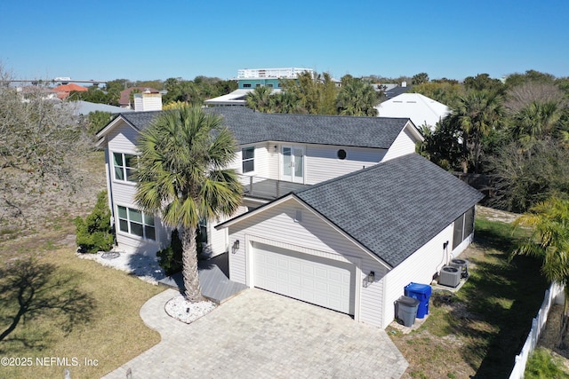 view of front of house featuring a shingled roof, decorative driveway, central AC unit, and a front yard