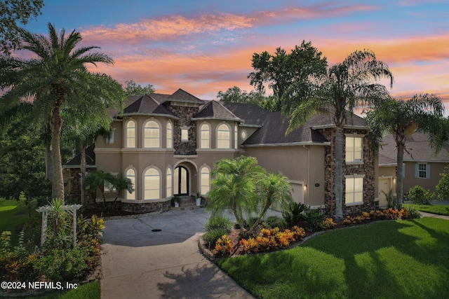 french country inspired facade featuring stucco siding, concrete driveway, an attached garage, stone siding, and a front lawn