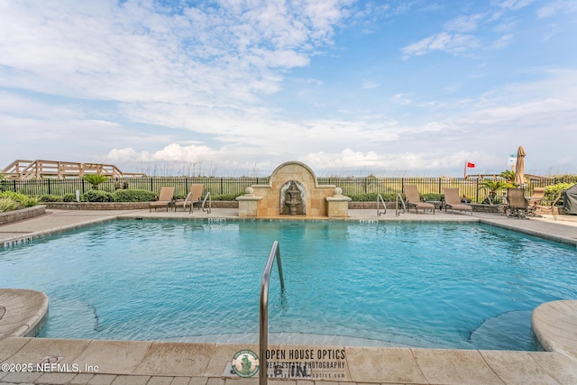 community pool with fence, exterior fireplace, and a patio