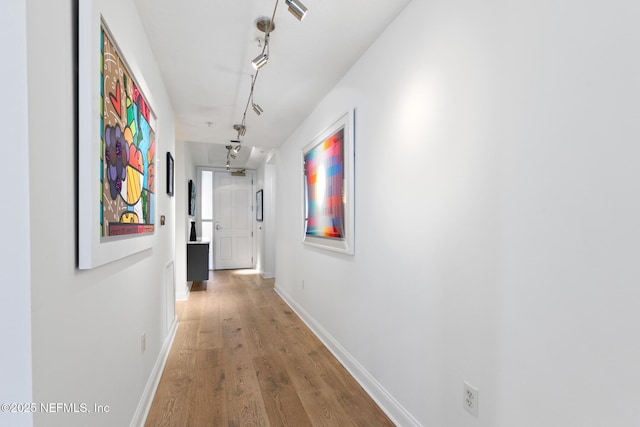 hall featuring rail lighting, baseboards, and wood finished floors