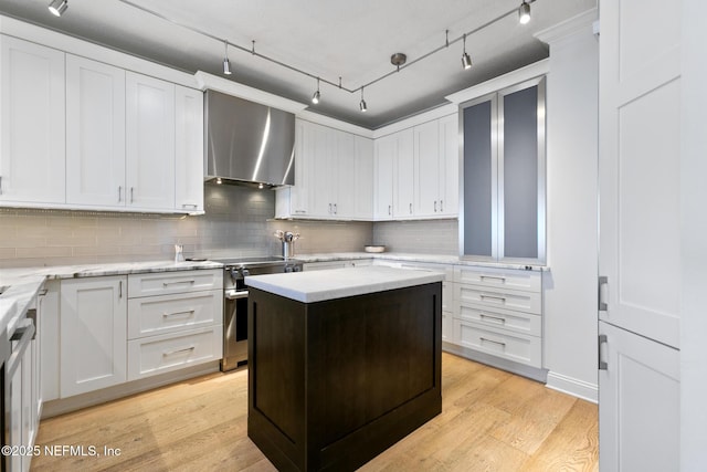 kitchen featuring tasteful backsplash, light wood-style floors, white cabinetry, wall chimney range hood, and stainless steel electric range