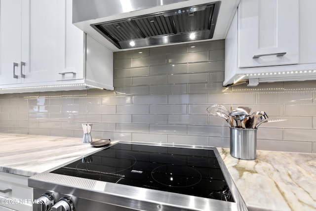 kitchen featuring stove, white cabinetry, ventilation hood, decorative backsplash, and light stone countertops