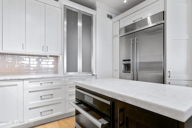 kitchen with tasteful backsplash, built in fridge, visible vents, and white cabinets