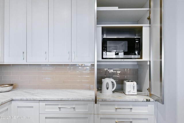 kitchen featuring light stone countertops, stainless steel microwave, white cabinets, and backsplash