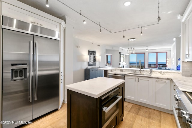 kitchen with white cabinets, a peninsula, stainless steel built in fridge, light wood-style floors, and a sink