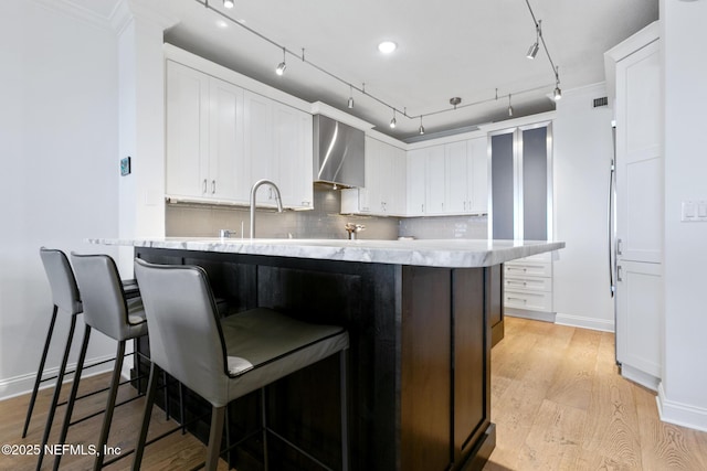 kitchen featuring a peninsula, light wood finished floors, backsplash, and white cabinetry