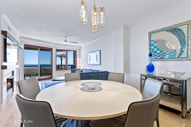 dining room featuring ornamental molding, ceiling fan with notable chandelier, a fireplace, and wood finished floors