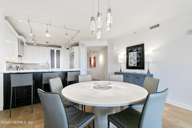 dining area with visible vents, light wood-style flooring, an inviting chandelier, ornamental molding, and baseboards