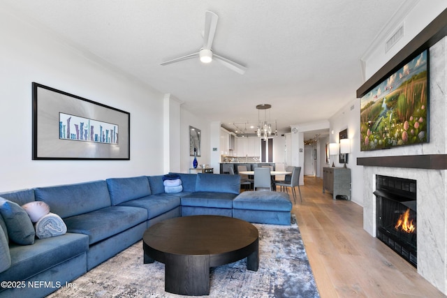 living area with light wood finished floors, ceiling fan with notable chandelier, visible vents, and a glass covered fireplace