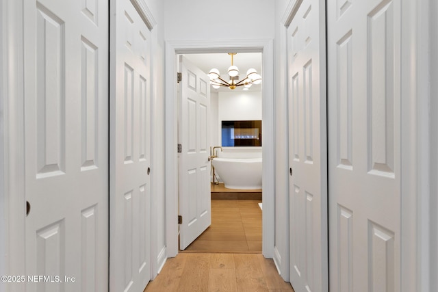 corridor featuring light wood-type flooring and an inviting chandelier