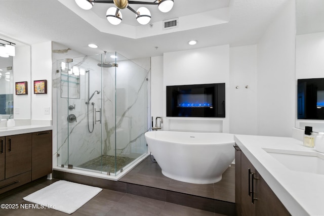 bathroom with a sink, two vanities, a soaking tub, a marble finish shower, and a raised ceiling