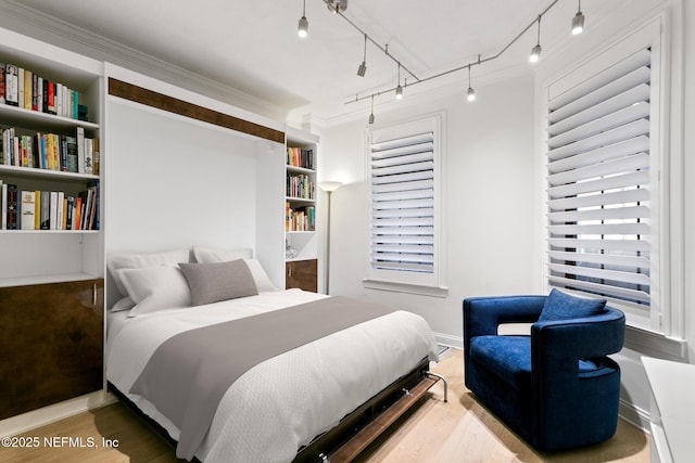 bedroom with ornamental molding, baseboards, track lighting, and wood finished floors