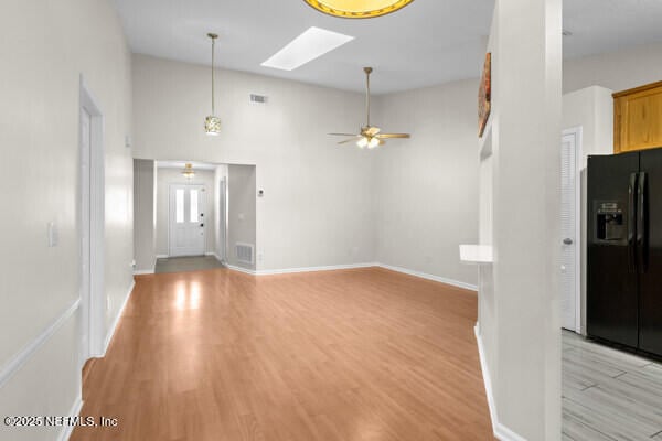 unfurnished living room with a skylight, a ceiling fan, visible vents, baseboards, and light wood-type flooring