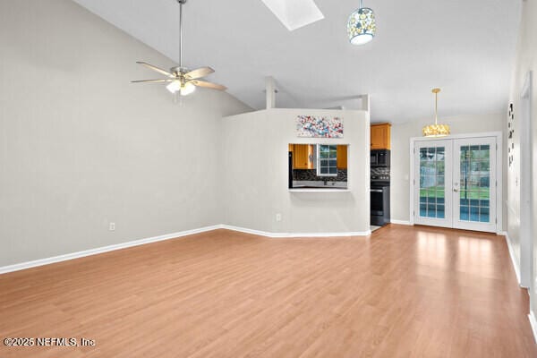 unfurnished living room with a ceiling fan, a skylight, light wood-style flooring, and baseboards