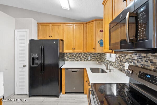 kitchen with lofted ceiling, a sink, light countertops, black appliances, and tasteful backsplash