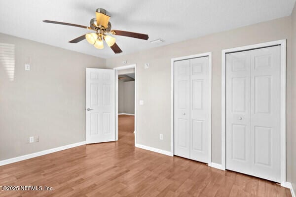 unfurnished bedroom with a ceiling fan, light wood-style flooring, baseboards, and two closets