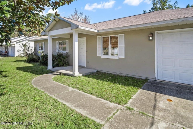 view of front of home with an attached garage, roof with shingles, a front yard, and stucco siding