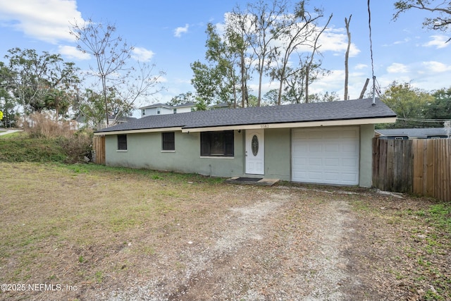 ranch-style home featuring an attached garage, fence, dirt driveway, roof with shingles, and stucco siding