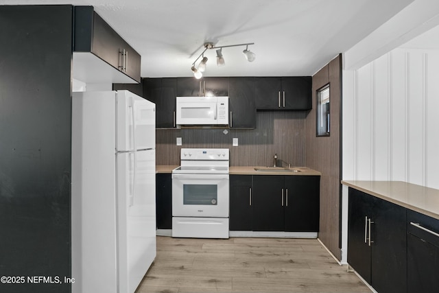 kitchen featuring white appliances, dark cabinetry, light wood finished floors, and a sink