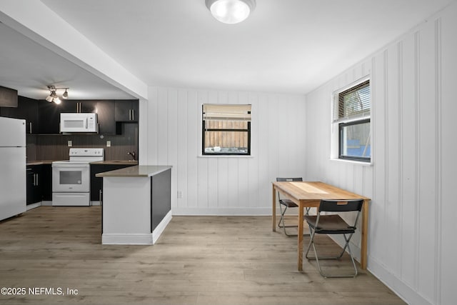 kitchen featuring light wood finished floors, a peninsula, white appliances, and a sink