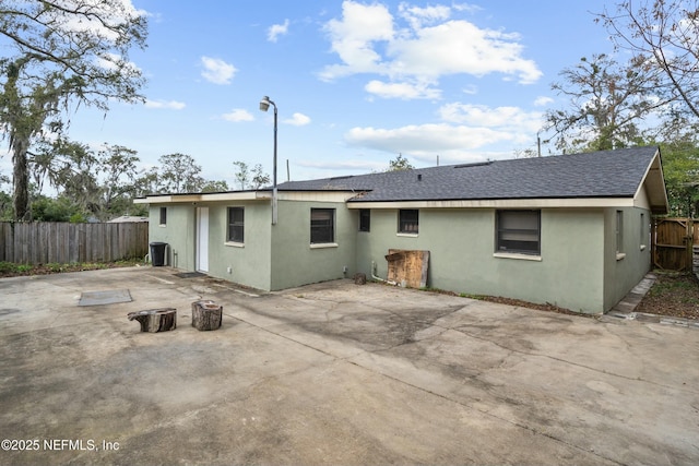 rear view of property featuring a patio, roof with shingles, fence, and stucco siding