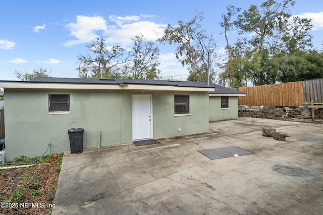 back of house featuring roof with shingles, a patio area, fence, and stucco siding