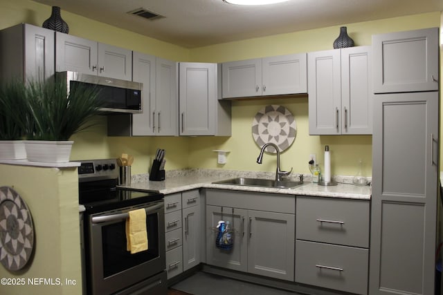 kitchen featuring visible vents, gray cabinets, stainless steel appliances, and a sink