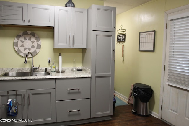 kitchen featuring gray cabinetry, dark wood-type flooring, baseboards, and a sink